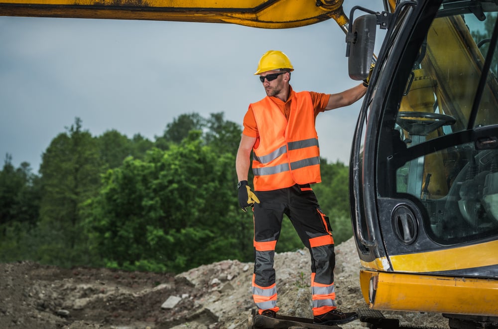 Machine Operator Standing on Hydraulic Excavator Assessing Job Site.